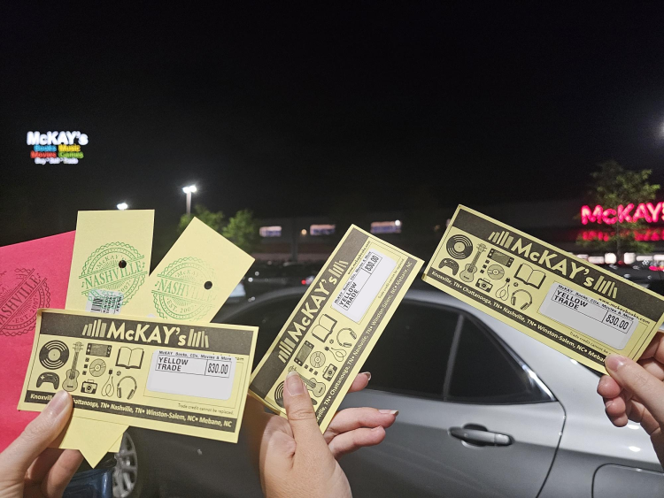 Photo of three hands holding up trade credit slips, plus three other slips with holes punched in them and a Nashville stamp each. The signs for the Nashville McKays glow in the distance.